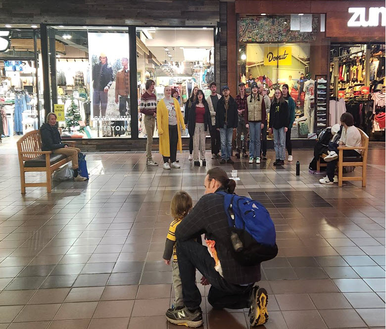 a group of men and women inside of the mall singing Christmas carols.