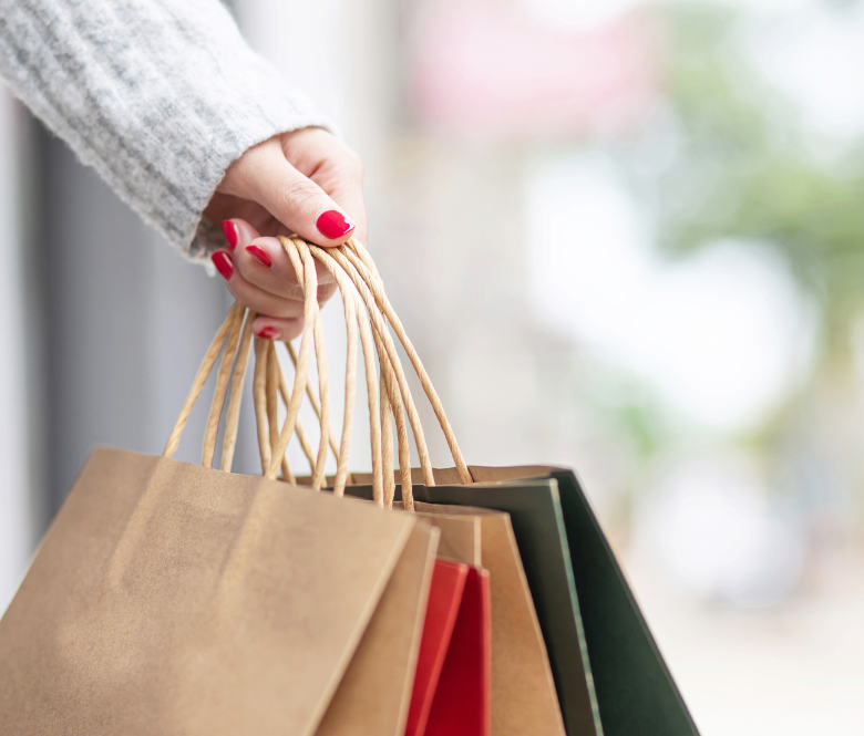 A hand with red painted fingernails holding a variety of shopping bags.