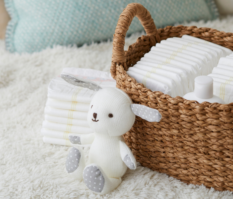 A stuffed animal propped up against a wicker basket filled with baby diapers.