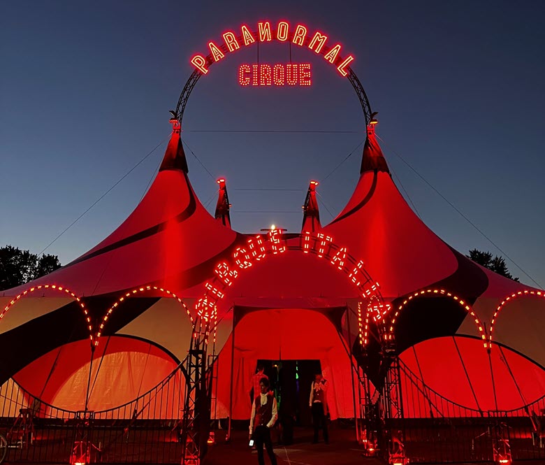 A circus tent lit up in red during the evening.