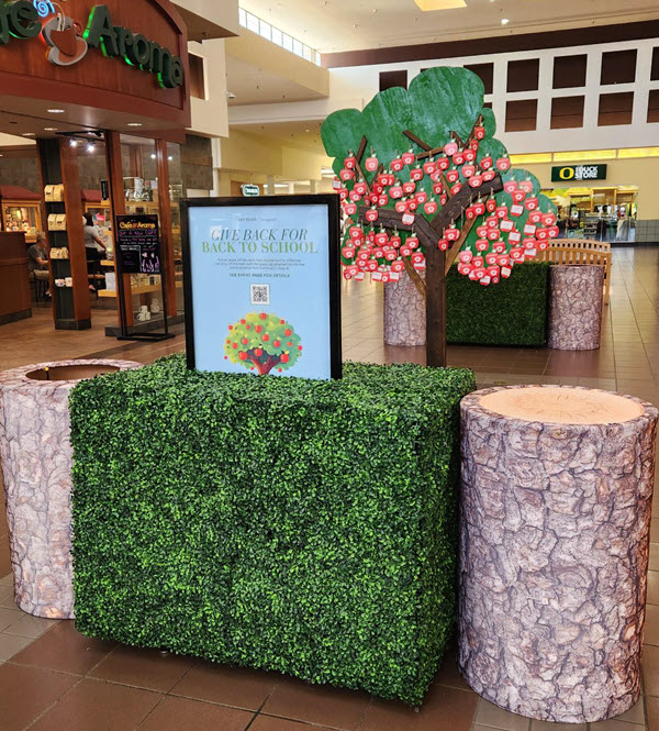 A wooden apple tree with apple tags and bins decorated for tree stumps for donation items.