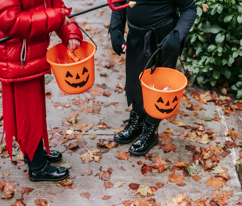 Two kids holding pumpkin shaped buckets with candy inside of them.