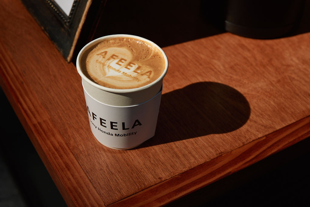 A cup of coffee on a desk with the words AFEELA on the cup