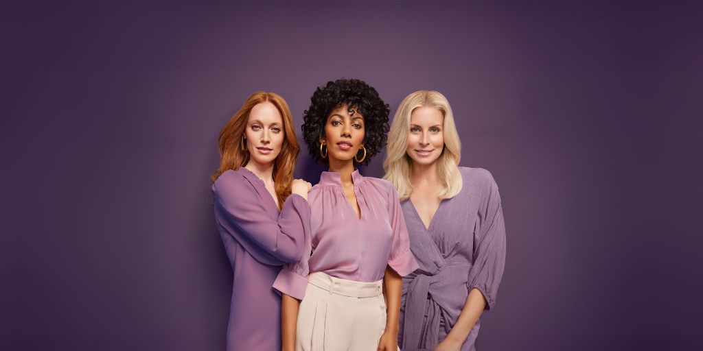 Three women all in purple standing against a purple wall