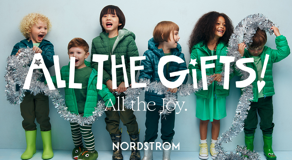 A group of kids smiling and laughing all dressed in green attire holding a piece of silver garland