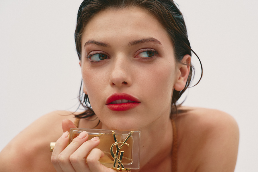 A woman with slicked back hair and red lipstick holiday a YSL perfume bottle