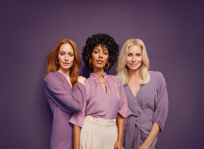 Three women all in purple blouses and dresses against a purple background.