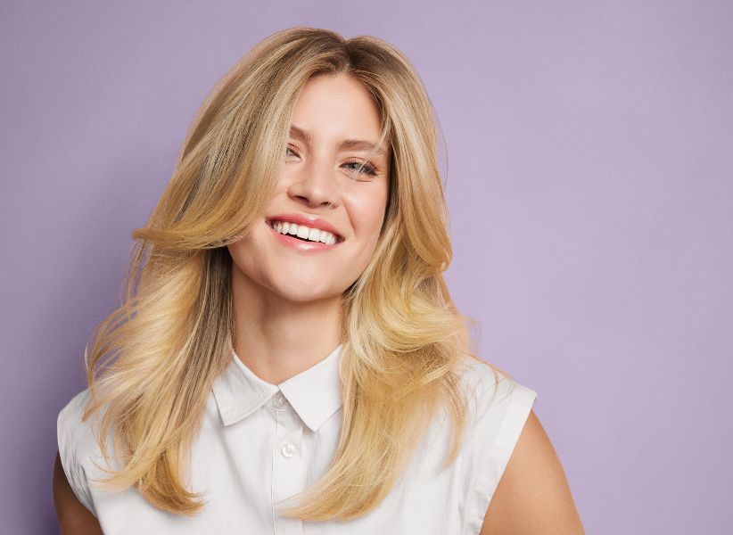 A blond woman in a white blouse against a purple background.