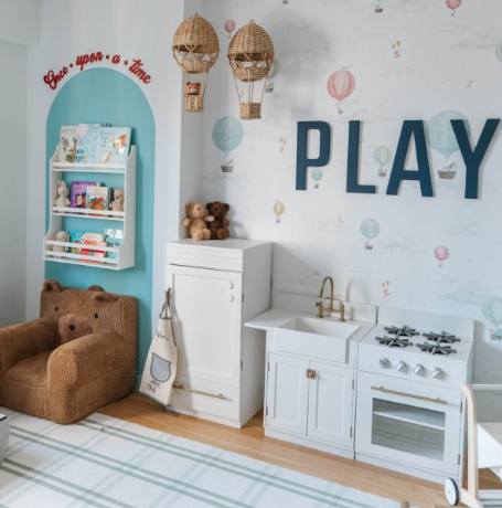 A kids room decorated with a play oven, refrigerator, bookshelf, brown bear chair and the word Play on the wall