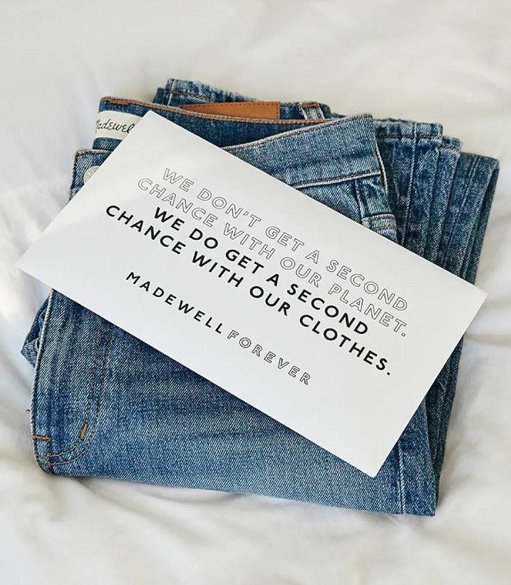 A stack of blue jeans with a card on top that says " we don't get a second chance with our planet. We do get a second chance with our clothes".