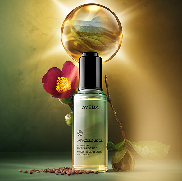 A bottle of Aveda's Miraculous Hair Oil against a green and brown backdrop