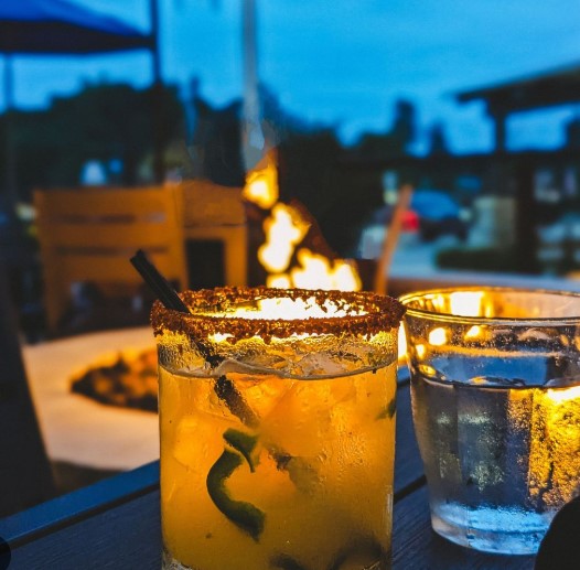 A cocktail with a seasoned rim on a table in front of a fire
