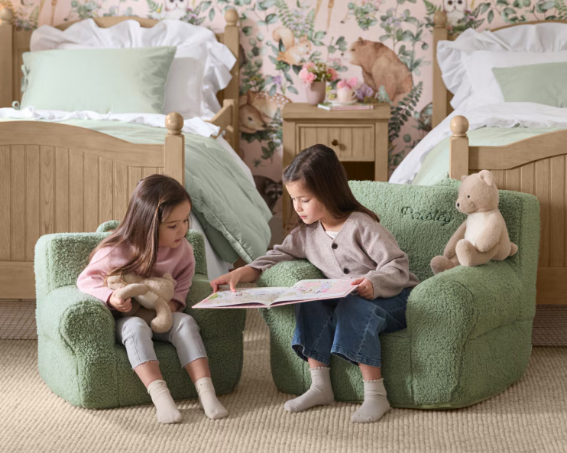 Two young girls reading a book, sitting on small green lounge chairs 