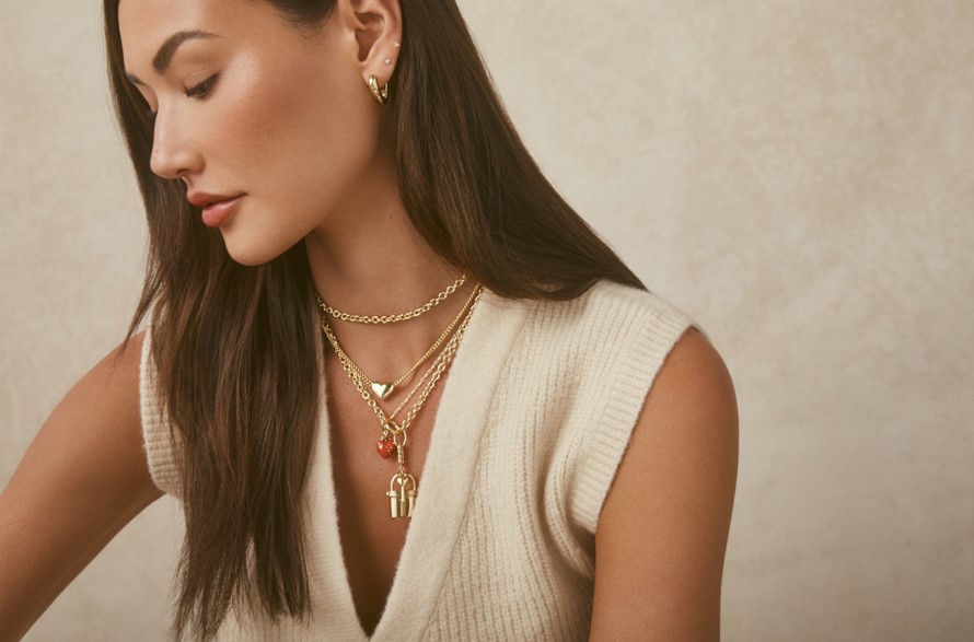 A brunette woman in a cream sweater wearing necklaces and earrings from Gorjana