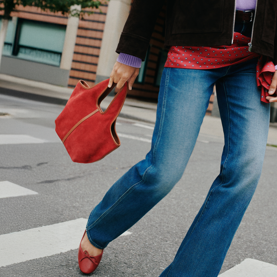 A girl walking on the street in blue jeans, wearing red shoes and carrying a red bag