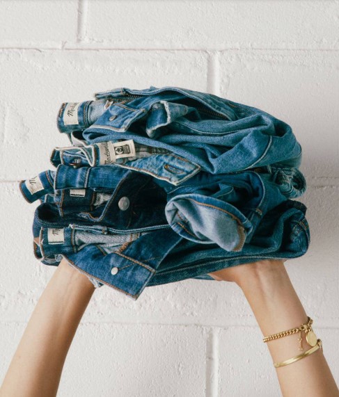 Woman's hands holding up stacked & folded blue jeans