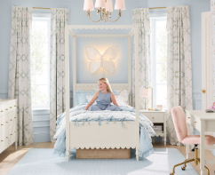 A little girl sitting on a blue and white bed in a beautifully decorated blue, white and pink room