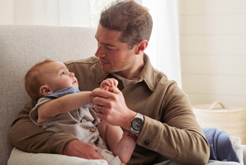 A dad sitting on a chair holding and talking to his baby