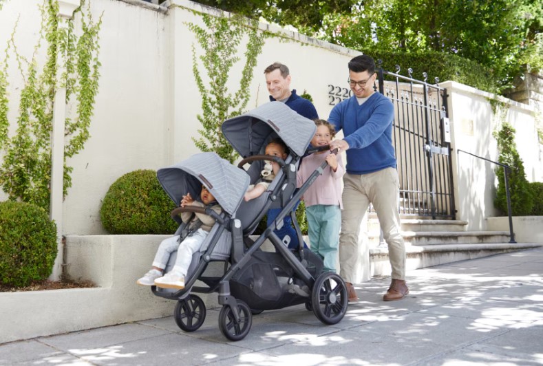Two dads walking down the sidewalk pushing their kids in strollers