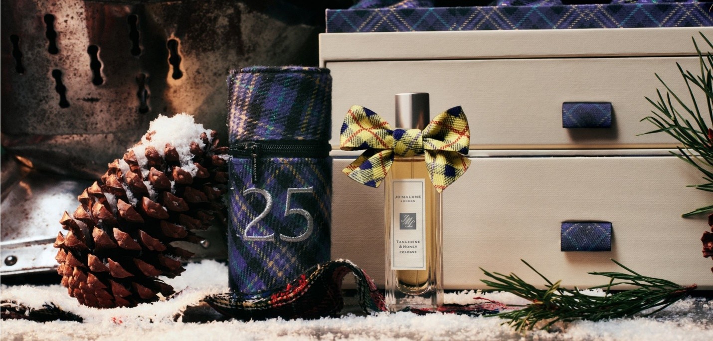 A Jo Malone fragrance bottle wrapped in ribbon with a pine cone next to it