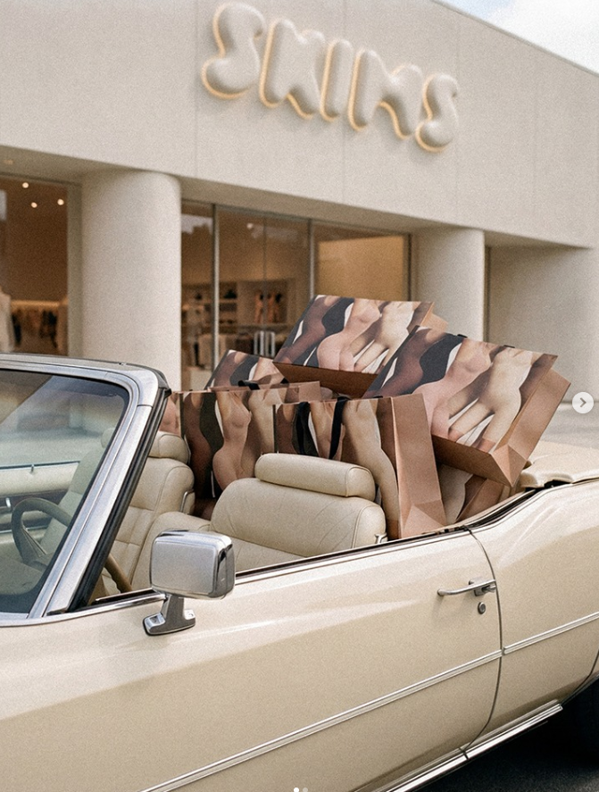 A convertible car with SKIMS bags in the back seat in front of a SKIMS store