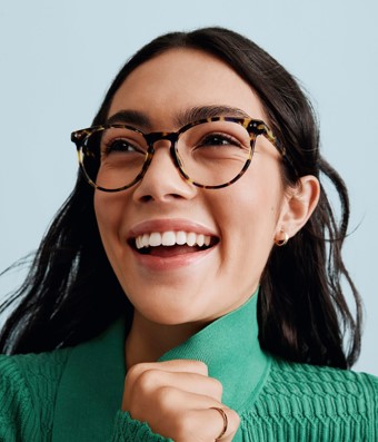A woman in a green sweater smiling and wearing frames from Warby Parker