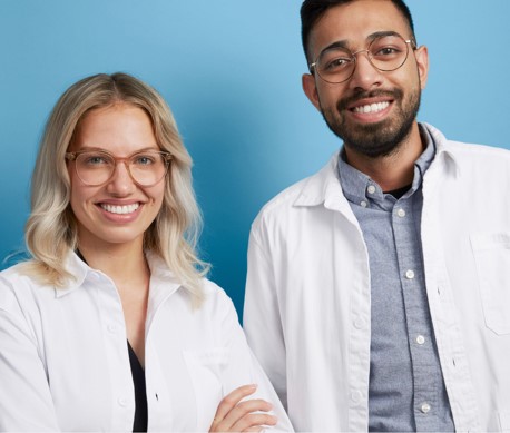 A blond woman and dark haired man wearing glasses and white lab coats