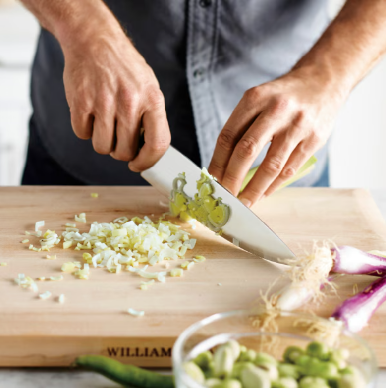 A man chopping onions with a knife on a cutting board branded Williams Sonoma