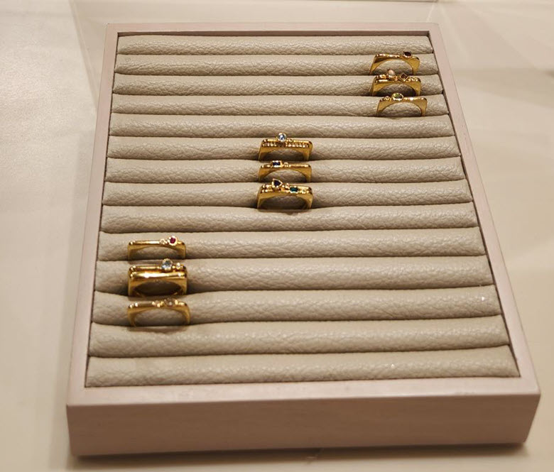 A jewelry display features multiple gold rings arranged neatly on a padded tray.