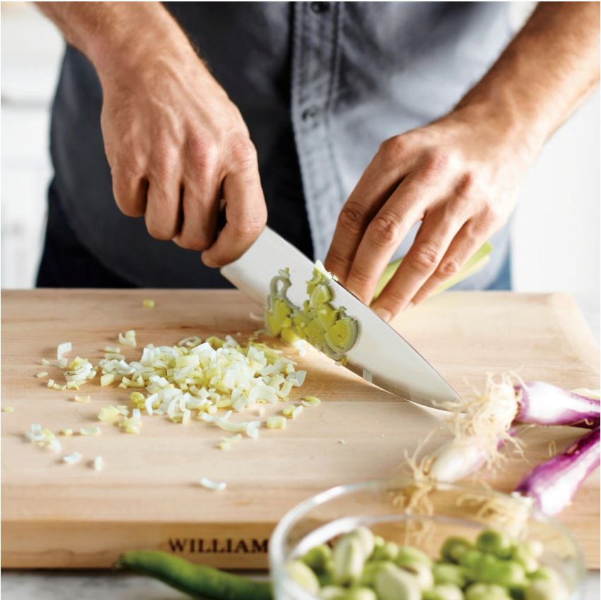 a man using a knife to chop onions on a Williams Sonoma cutting board