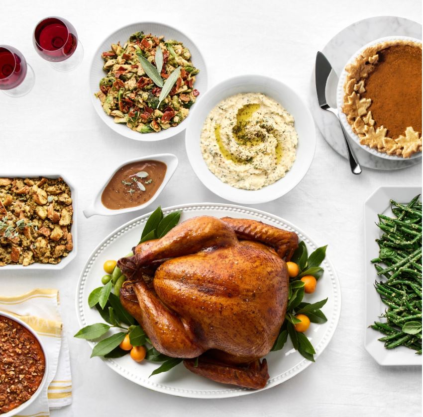 A Thanksgiving dinner table picture with turkey, stuffing, vegetables, pies and more