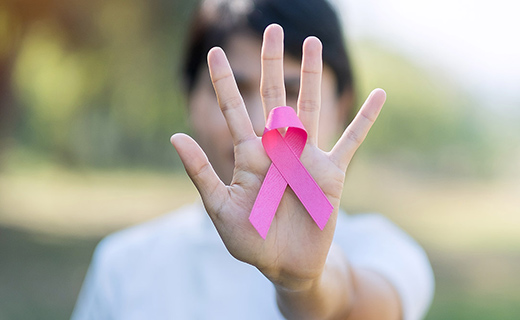 Person displaying pink ribbon on her hand.