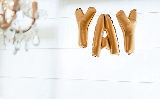  white wall with gold bubble balloons spelling out the word yay.