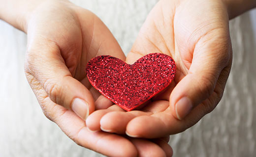 Two hands holding a glittered paper heart