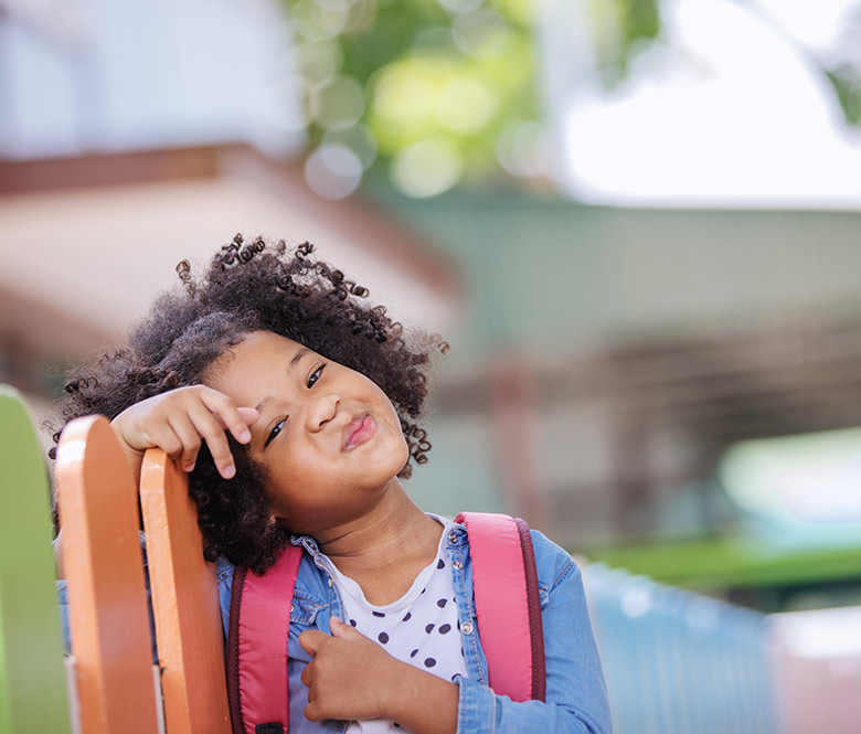 school girl leaning on fence with backpack on.