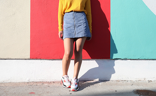 image of girl in jean skirt leaning against yellow wall