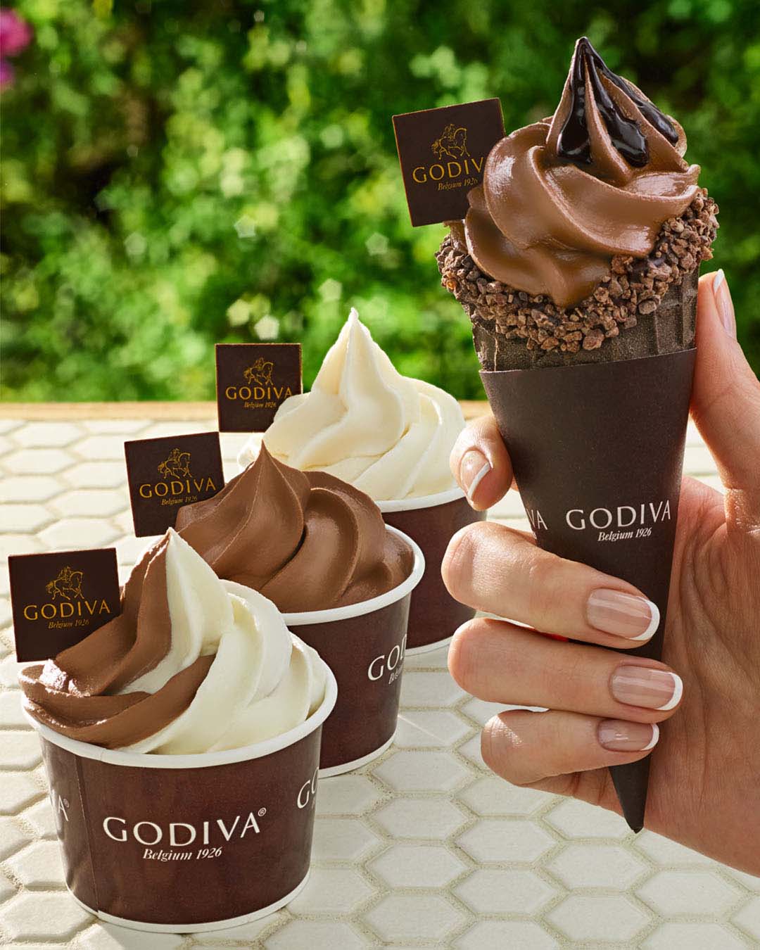 Shown three Soft Serve ice cream cups one each chocolate/vanilla swirl, chocolate and vanilla and chocolate soft serve topped with chocolate syrup in a waffle cone