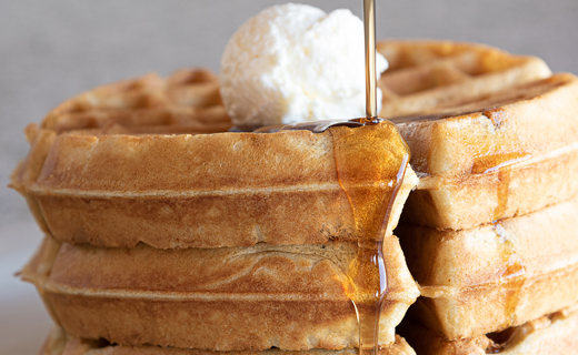 Stacked waffles with ball of butter on top and syrup pouring