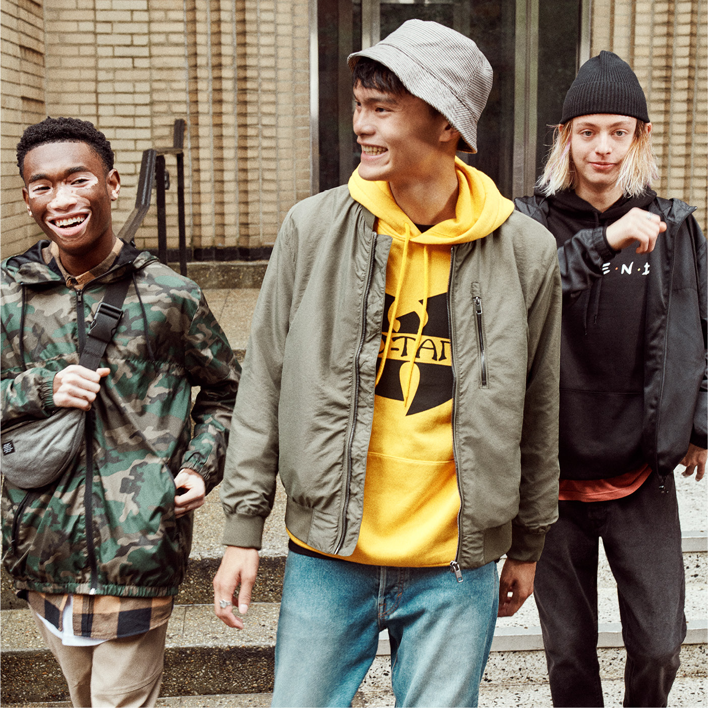 Three teen boys, wearing jackets, two with hats walking together one with fanny pack around his shoulder walking down stairs.
