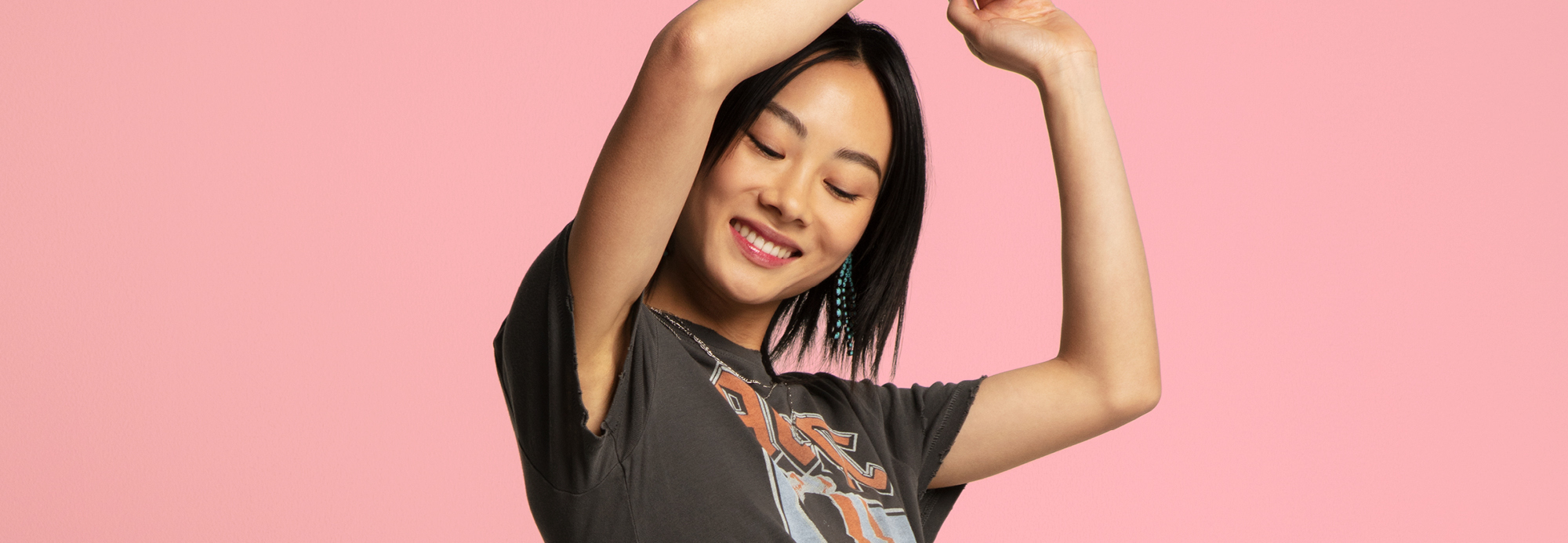 Girl raising her arms up and smiling. Background is pink.