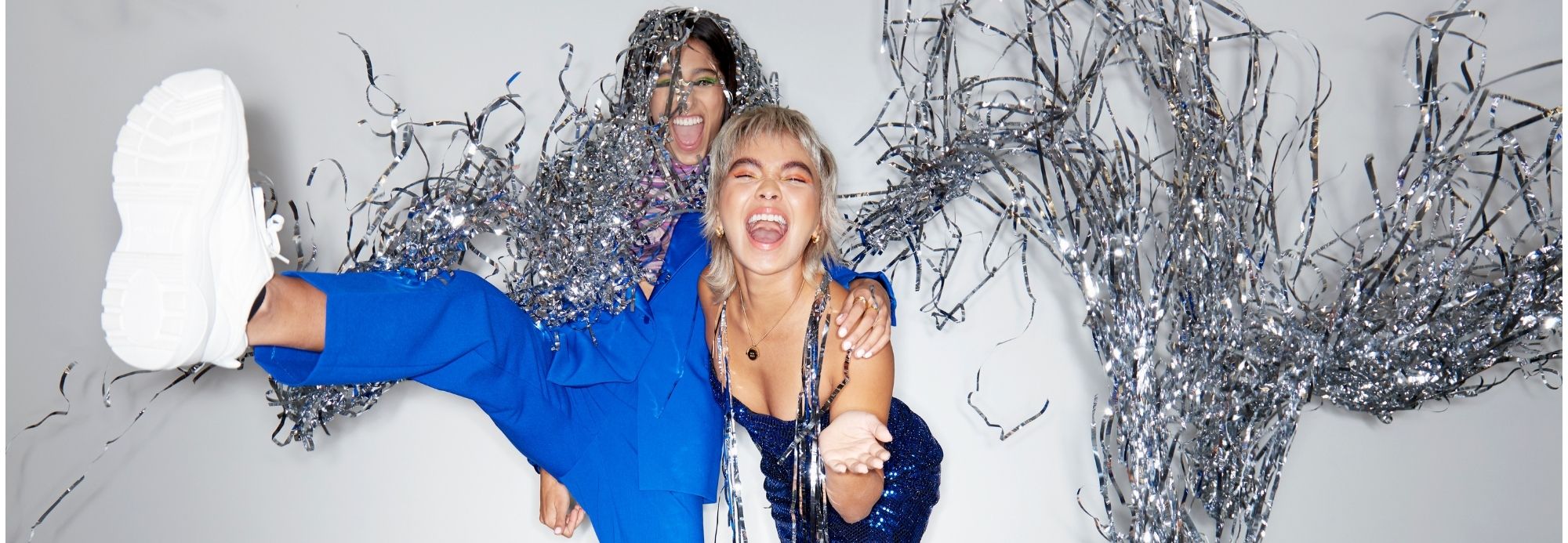 Two women with their arms around one another joyously laughing with silver streamers blowing around them