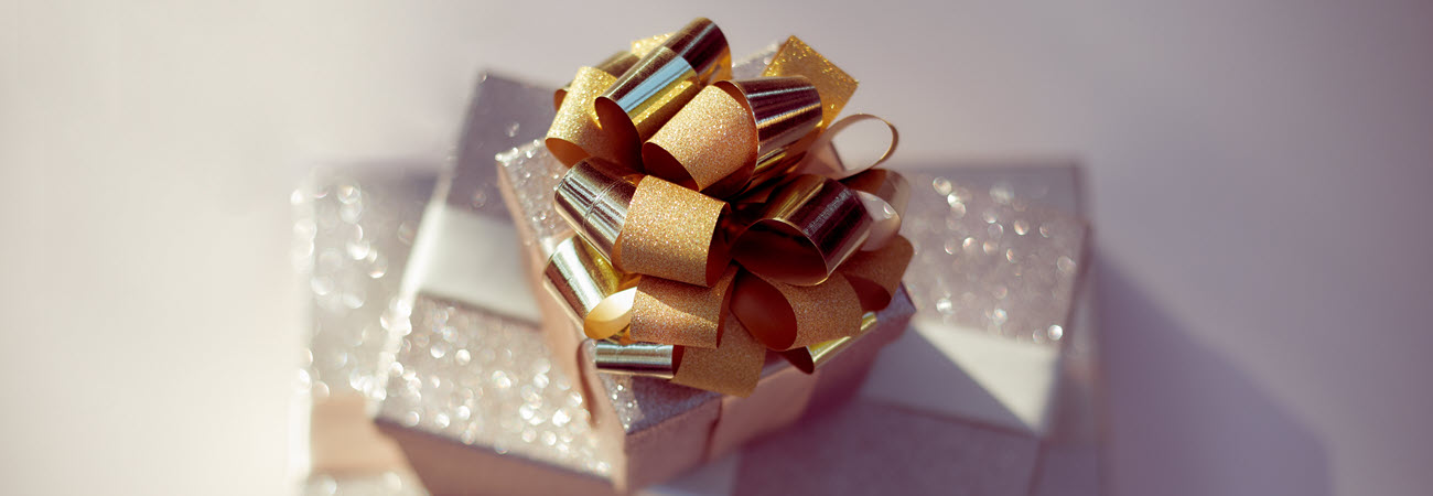 A glittery stack of present in metallic wrapping paper with a gold bow on top