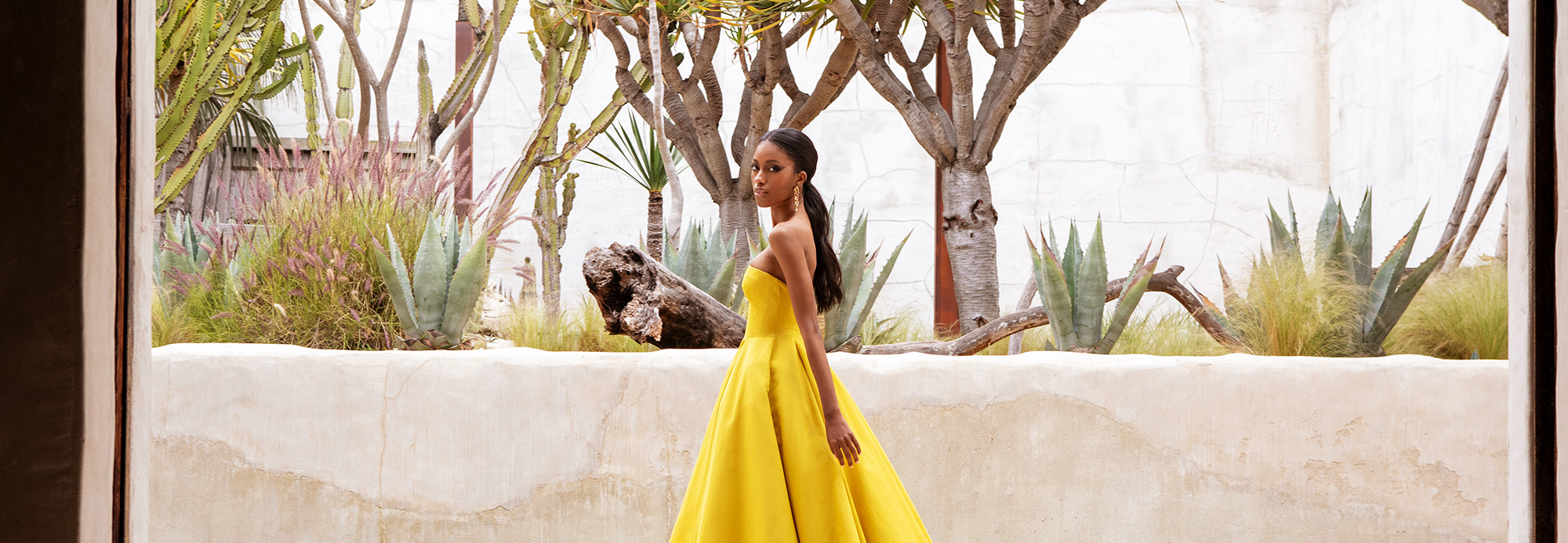 Female model wearing a yellow dress standing in front of desert plants