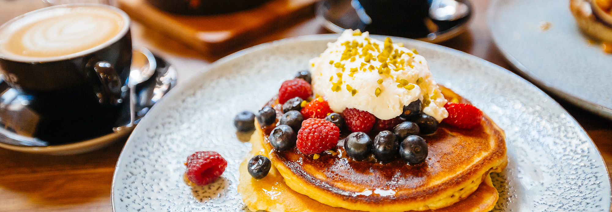 Pancakes topped with berries and cream served with lattes on a restaurant table