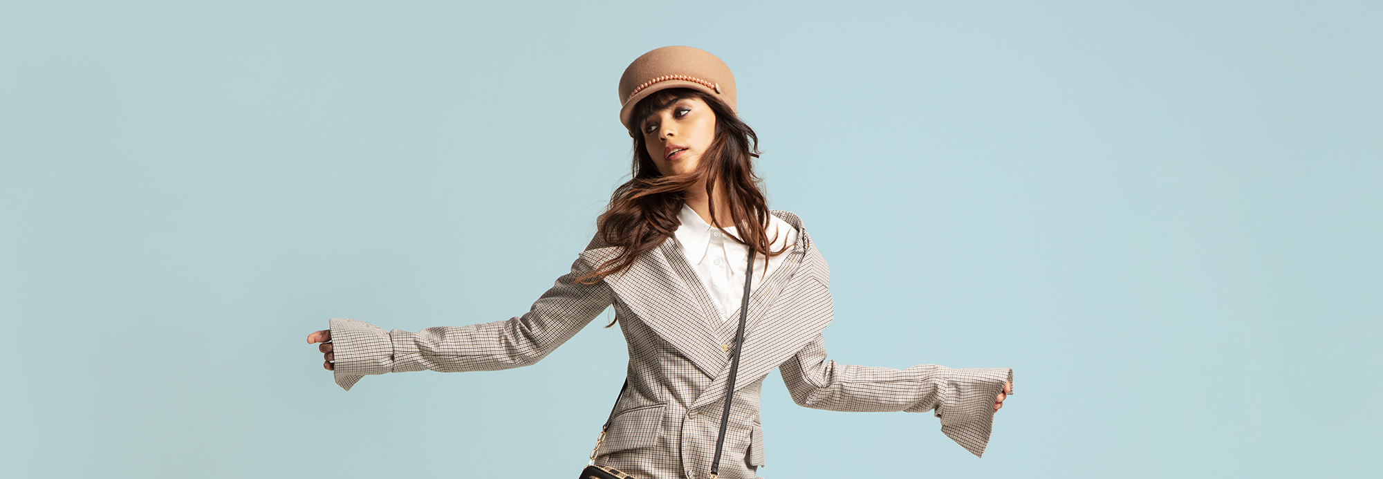A young woman in a trendy oversize blazer and conductor's hat striking a pose