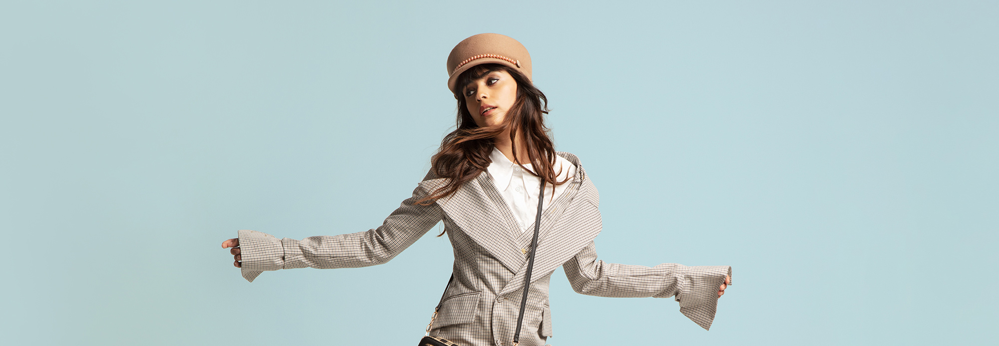 A young woman striking a pose and wearing a statement blazer with flared sleeves and a conductors hat.