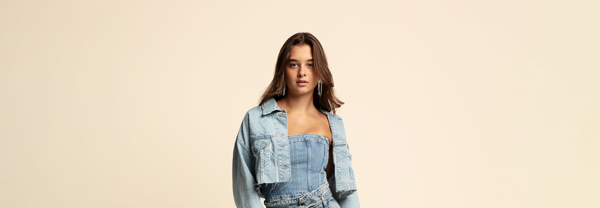 A young woman wearing a denim cropped jacket and denim sleeveless jumpsuit