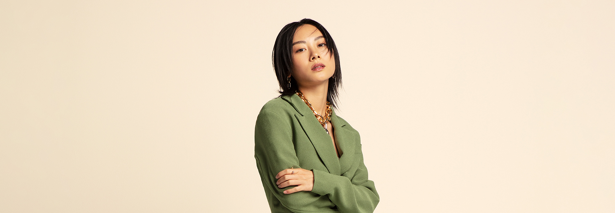 A stylish young woman wearing a green blazer and chunky gold chain necklace