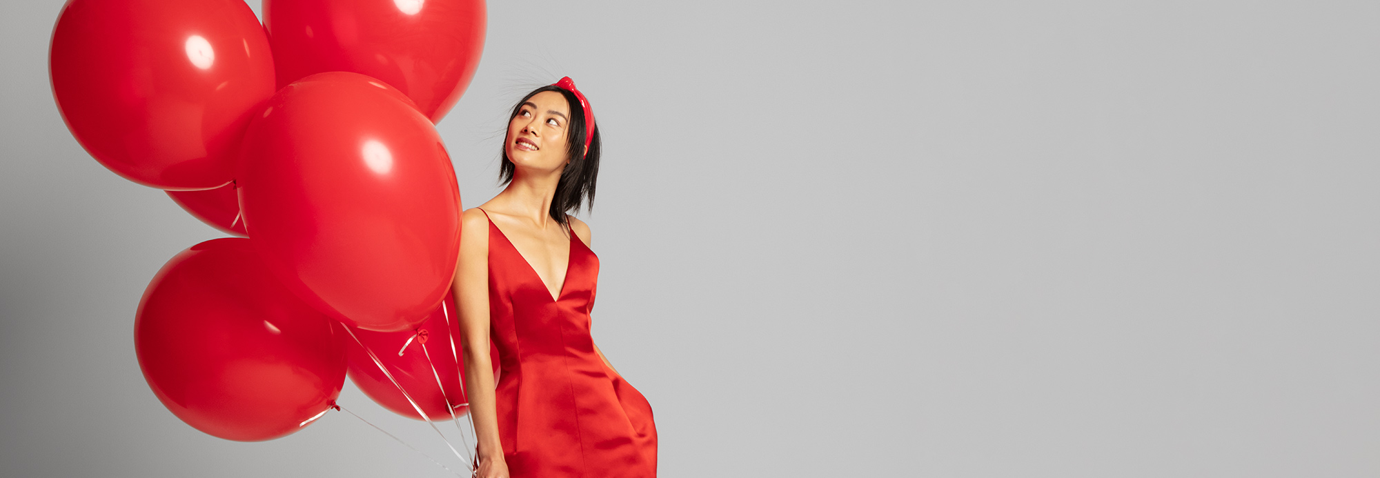 A woman in a red party dress holding red balloons