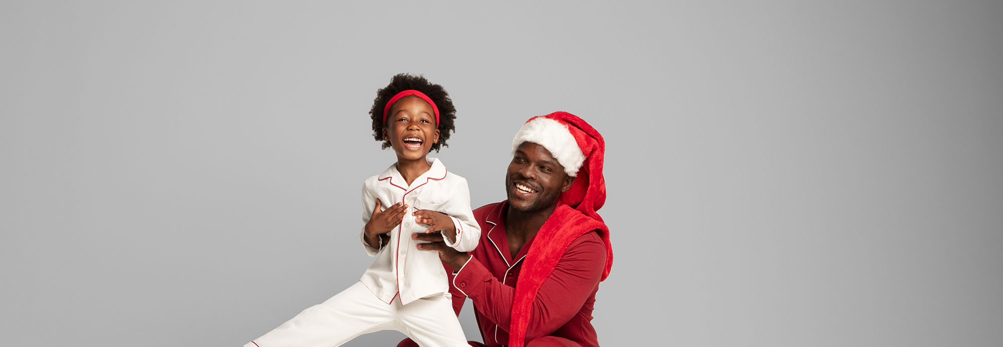 A father in red pajamas and a Santa hat holding up his child